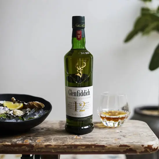 Бутилка 12-годишно скоч уиски Glenfiddich 1 л. върху маса с 1 чаша с уиски